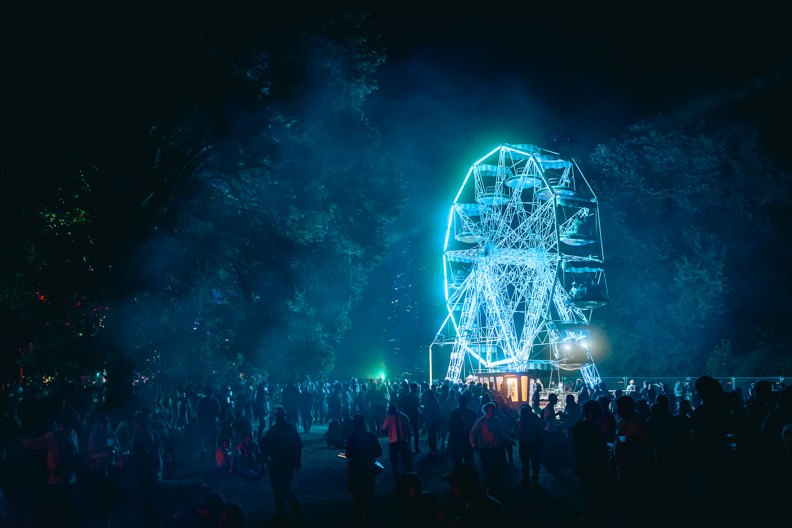 Une grande roue éclairée de bleu surplombe les festivaliers dans la nuit.