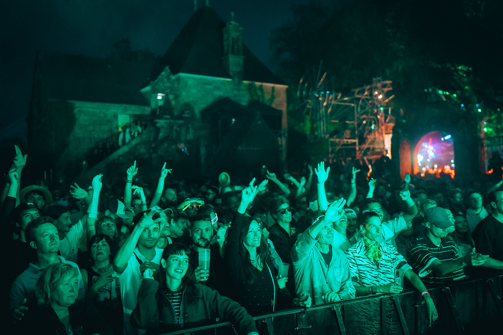Le public du festival, les mains levées sous une lumière verte.