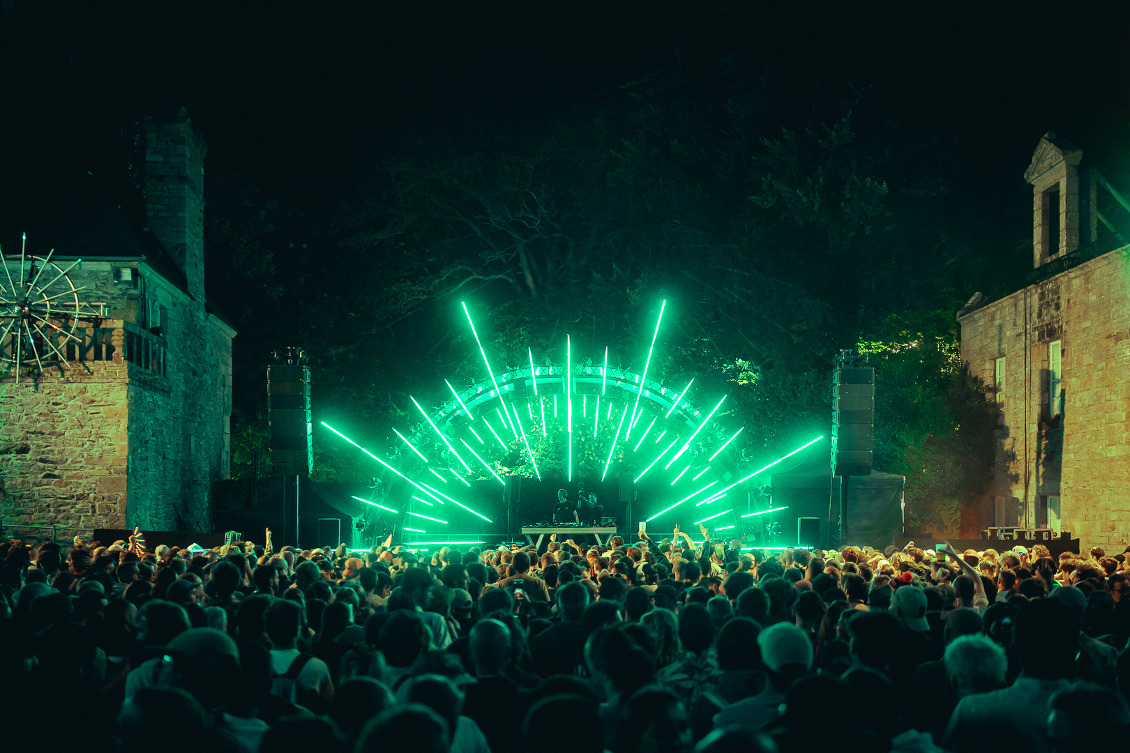 La scène d’Astropolis illuminée de vert, devant une foule entre deux bâtiments en pierre.